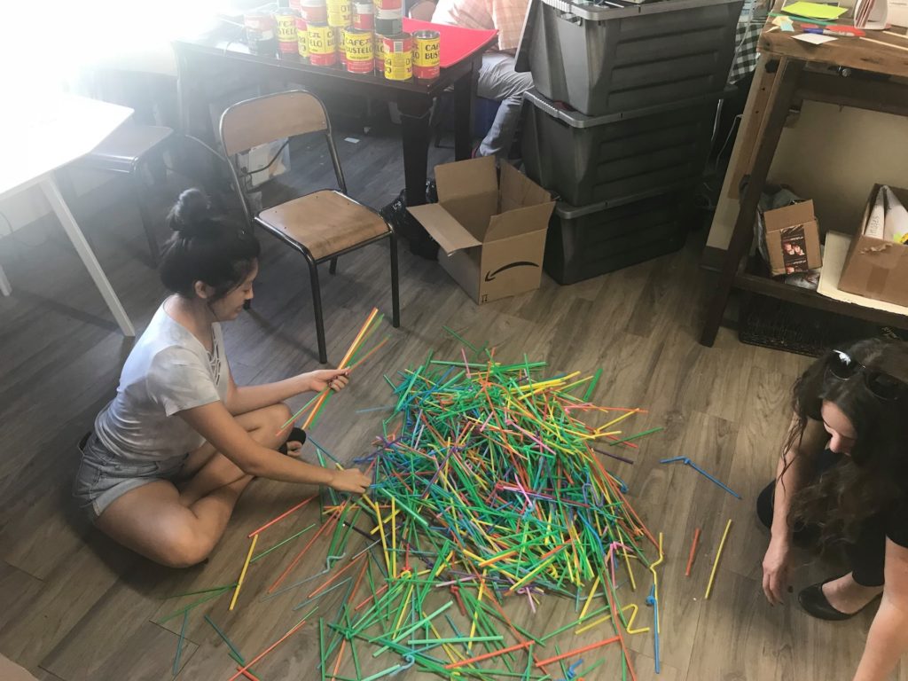 People sitting on an office floor sorting used straws by size and color